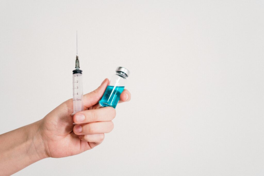 pexels-photo-3952241-3952241 Hand holding a syringe and vaccine vial on a white background, symbolizing healthcare and immunization.